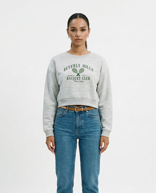 Vintage-inspired cropped crewneck sweatshirt for women featuring a relaxed fit, classic crew neckline, and collegiate racquet club graphic, styled on a model against a white studio background.