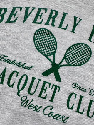 Front view of a cropped women’s crewneck sweatshirt highlighting the relaxed silhouette, long sleeves, and vintage racquet club chest graphic.