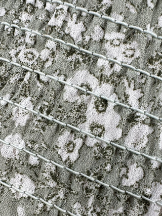 Close-up of green floral smocked fabric highlighting the textured stretch knit, small floral print, and soft elastic construction.