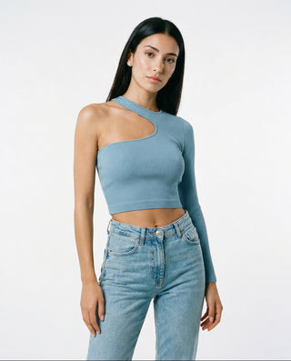Woman modeling a fitted dusty blue asymmetrical crop top with one long sleeve and ribbed stretch fabric