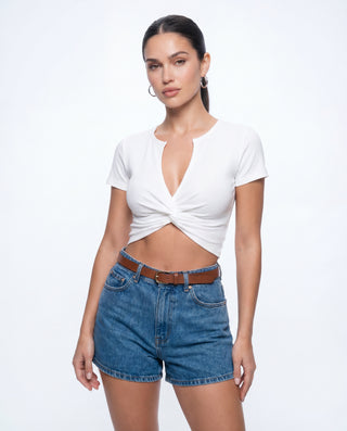 Women's white ribbed cropped top with a twist front detail, plunging V-neck, and short sleeves paired with denim shorts