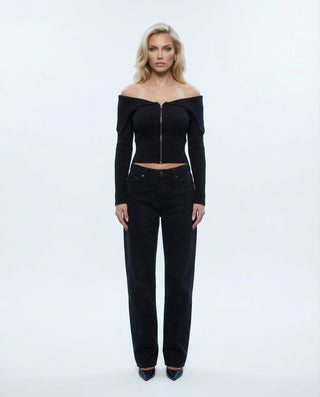 Blonde model in black off shoulder top and black jeans against a white backdrop.