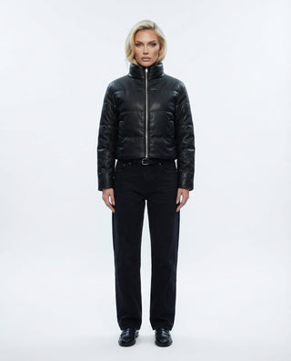 Blonde model in black puffer jacket styled with black jeans and loafers against a white back drop.