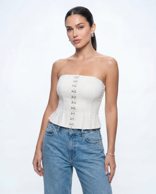 Women's white strapless corset top with hook-and-eye fastening, structured bodice, peplum hem, and fitted silhouette paired with light wash denim jeans