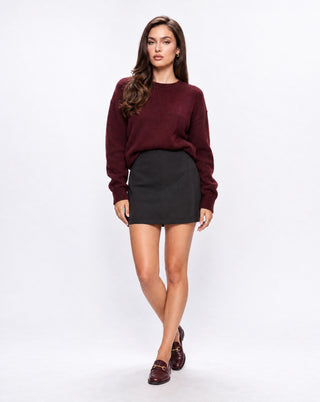 Women’s black high-waisted mini skirt styled with an oversized burgundy knit sweater and loafers, a chic fall outfit for brunch, workdays, city outings and everyday wear.