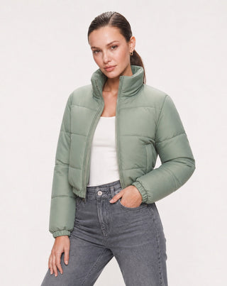 Women's sage green cropped puffer jacket with a high stand collar, zip front closure, quilted design, and lightweight insulated finish styled with gray jeans