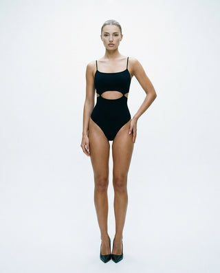 Black cutout bodysuit for women featuring thin shoulder straps, a scoop neckline, front waist cutout detail, high-cut leg openings, and a sleek body-hugging fit, styled on a model against a white studio background.