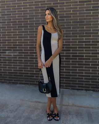 Model wearing black and cream striped dress, accessorized with gold jewelry, a black bag and black Hermes slippers.