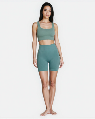 Woman wearing a green ribbed sports bra and shorts set on a white background