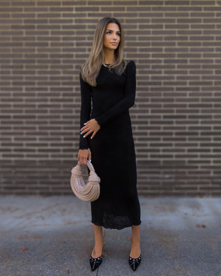 Model wearing a black sheer maxi dress and kitten heels while holding a cream bag.