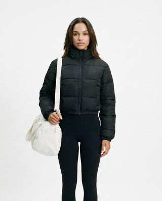 Women’s cropped puffer jacket with a high collar and quilted design, styled on a model fully zipped against a white studio background.