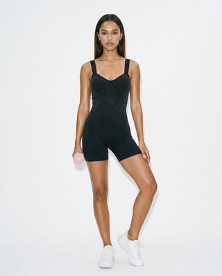 Black ribbed fitted romper for women featuring wide shoulder straps, contoured bust seams, mid-thigh length, and a smooth body-hugging silhouette, styled on a model against a white studio background.