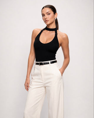 Women's black ribbed halter bodysuit with choker neckline, scoop neck, open shoulder design, and fitted silhouette styled with high waisted white wide leg trousers