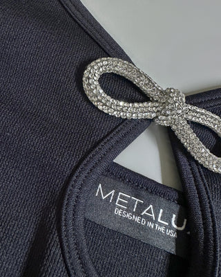 Close-up detail of a black crop top for women showing smooth stretch fabric, front keyhole opening, and crystal bow embellishment.