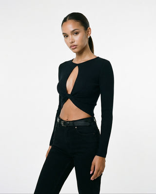 Model wearing a black ribbed long sleeve crop top with a front cutout and twisted center detail, styled with high-waisted black jeans against a clean white background.