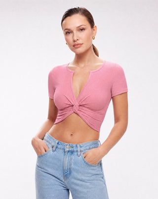 Women's dusty pink fitted crop top featuring a ribbed knit texture, twist front detail, V-neck, short sleeves, and cropped silhouette paired with light wash denim