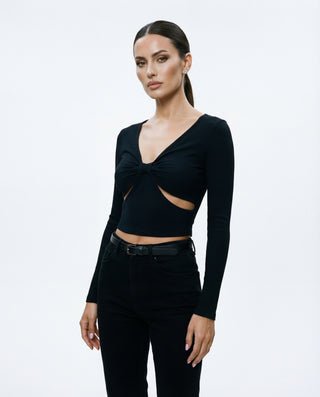 Model wearing a black ribbed long sleeve crop top with a twisted front detail and waist cutout, styled against a white background.