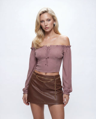 Women's dusty mauve off-the-shoulder crop top with long sleeves, gathered bust detail, and front tie neckline paired with a brown faux leather mini skirt