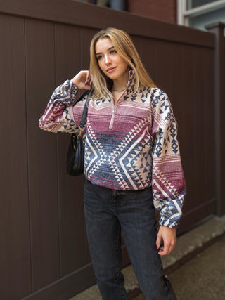 Model wearing a geometric red, blue and cream women's pullover sweater cardigan with black jeans while holding a black bag.