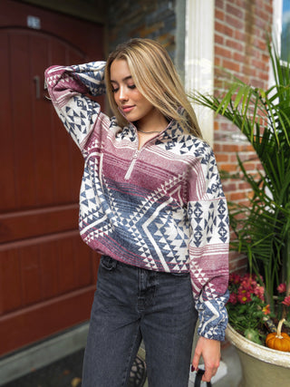 Model wearing a geometric red, blue and cream women's pullover sweater cardigan with black jeans while holding a black bag.