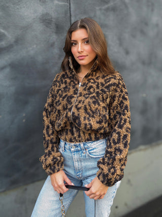 Model wearing leopard print fuzzy women's zip up cardigan with light wash blue jeans while holding a black bag.