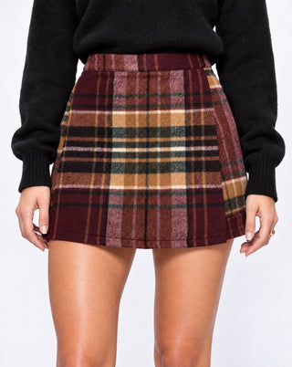 Close-up of women’s burgundy plaid pleated mini skirt with warm brown, cream and forest green checks, a preppy fall staple for brunch, coffee dates, campus style and weekend outfits.