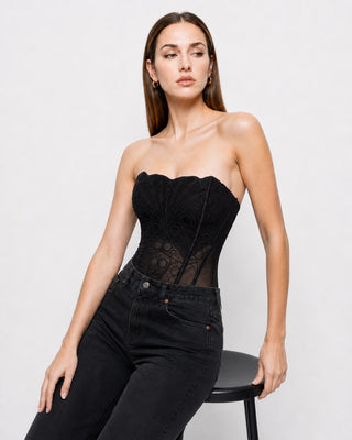 Women’s black lace strapless corset top with sheer mesh waist, structured boning and scalloped neckline, styled with black denim for a chic going-out, date night and fall evening outfit.