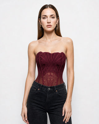 Front view of women’s burgundy lace corset top with strapless neckline, sheer mesh waist and structured boning, styled with black denim for elevated nightlife and fall fashion.