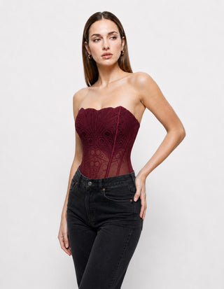 Women’s burgundy lace strapless corset top with sheer mesh panels and structured boning, styled with black jeans for a chic date night, evening and going-out outfit.