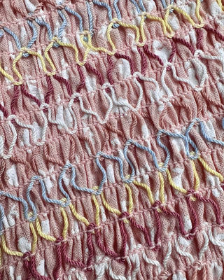 Close-up of the pastel multicolor smocked woven fabric on the mini dress, highlighting the textured smocking, woven detailing, and soft stretch finish.