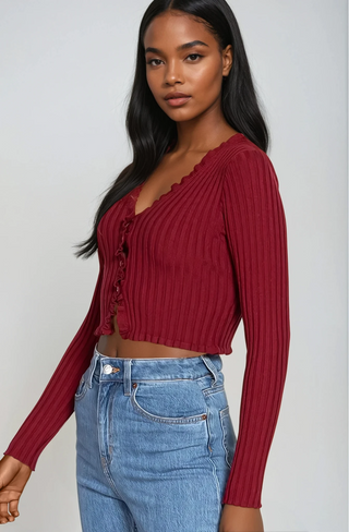 Woman wearing a red ribbed sweater and blue jeans against a plain background