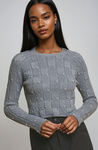Woman wearing a gray textured sweater with embellishments on a plain background