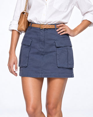 Close-up of women’s slate blue cargo mini skirt with oversized utility pockets, styled with a white button-down and tan belt for casual fall outfits, city days, brunch and weekend wear.